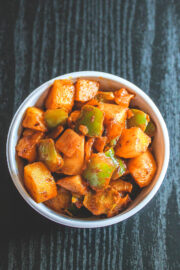 A bowl of aloo shimla mirch sabzi on a black board.