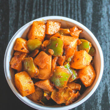 A bowl of aloo shimla mirch sabzi on a black board.