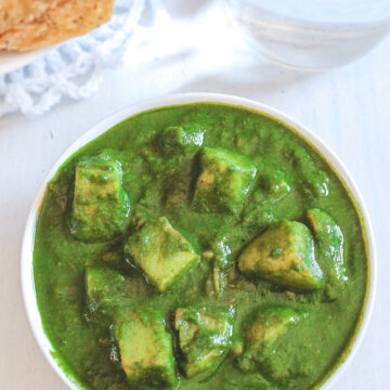 Aloo palak served in a bowl with paratha and a glass of water in the back.