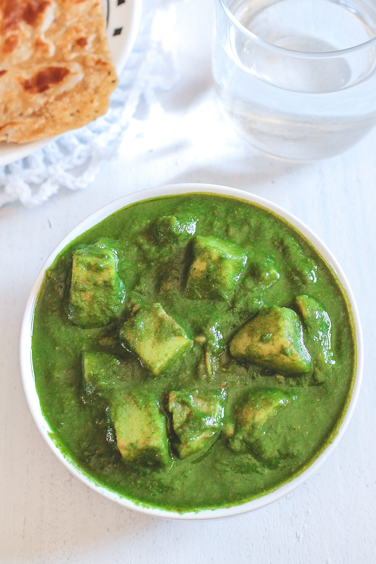 Aloo palak served in a bowl with paratha and a glass of water in the back.