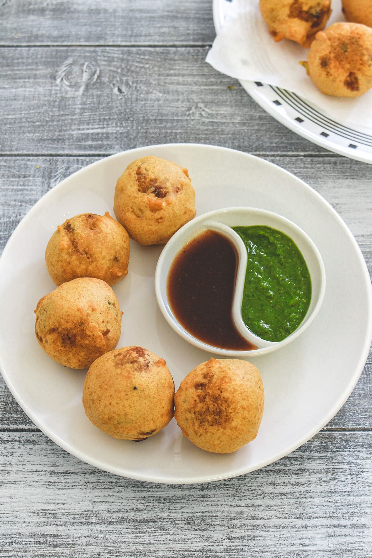 Batata vada in a plate with green chuney and tamarind date chutney.