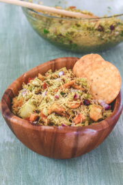 Bhel puri in a wooden bowl with 2 papdi on side and more bhel in the back.