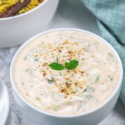 Cucumber raita garnished with mint leaves and cumin powder served with pulao.