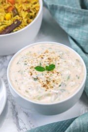 Cucumber raita garnished with mint leaves and cumin powder served with pulao.