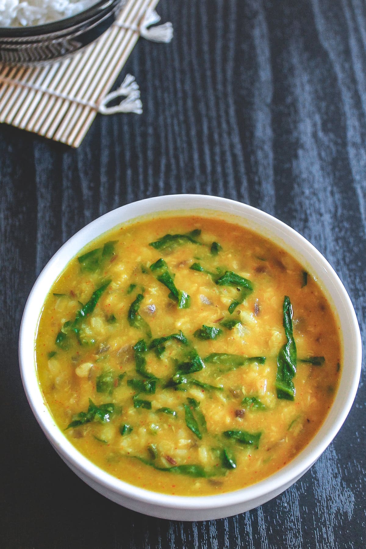 Dal palak served in a white bowl with rice in the back.