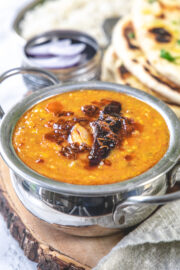 Dal tadka bowl on a wooden board, served sliced onion, rice and naan.