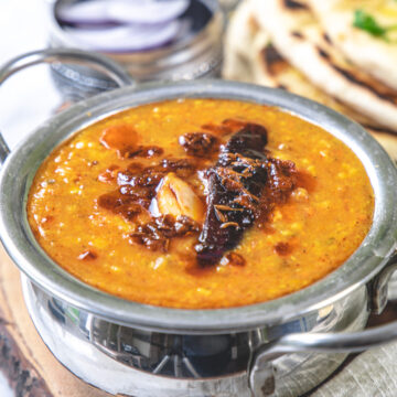 Dal tadka bowl on a wooden board, served sliced onion, rice and naan.