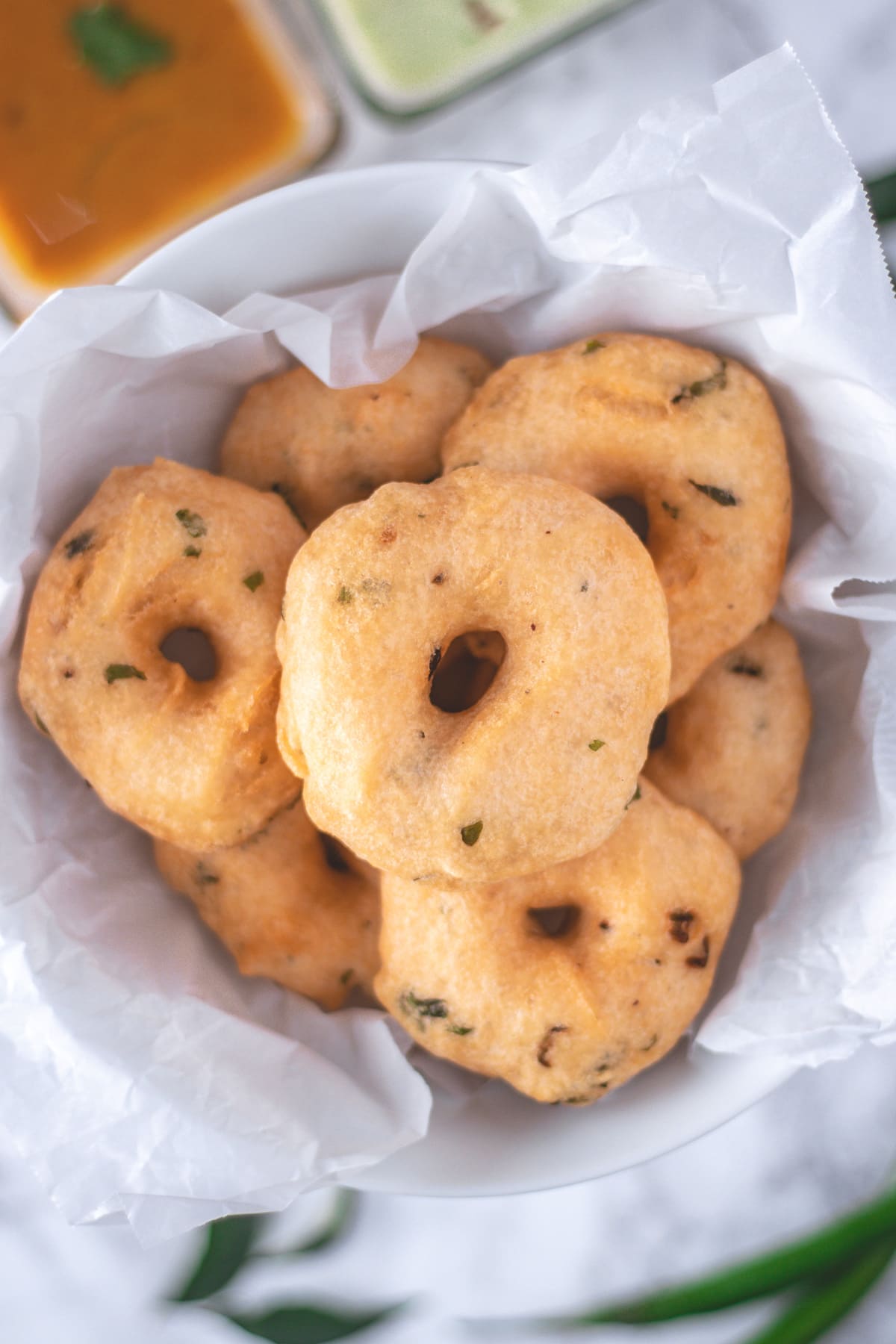 A parchement paper lined bowl is filled with medu vada.