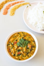 Methi dal served in a bowl with a plate of rice in the back.