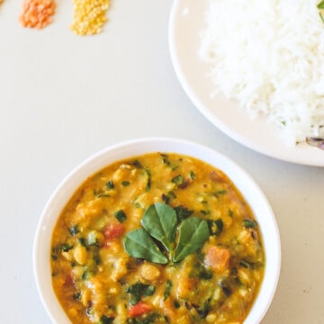 Methi dal served in a bowl with a plate of rice in the back.