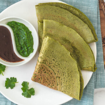 3 triangular folded moong dal chilla with cilantro chutney and tamarind chutney.