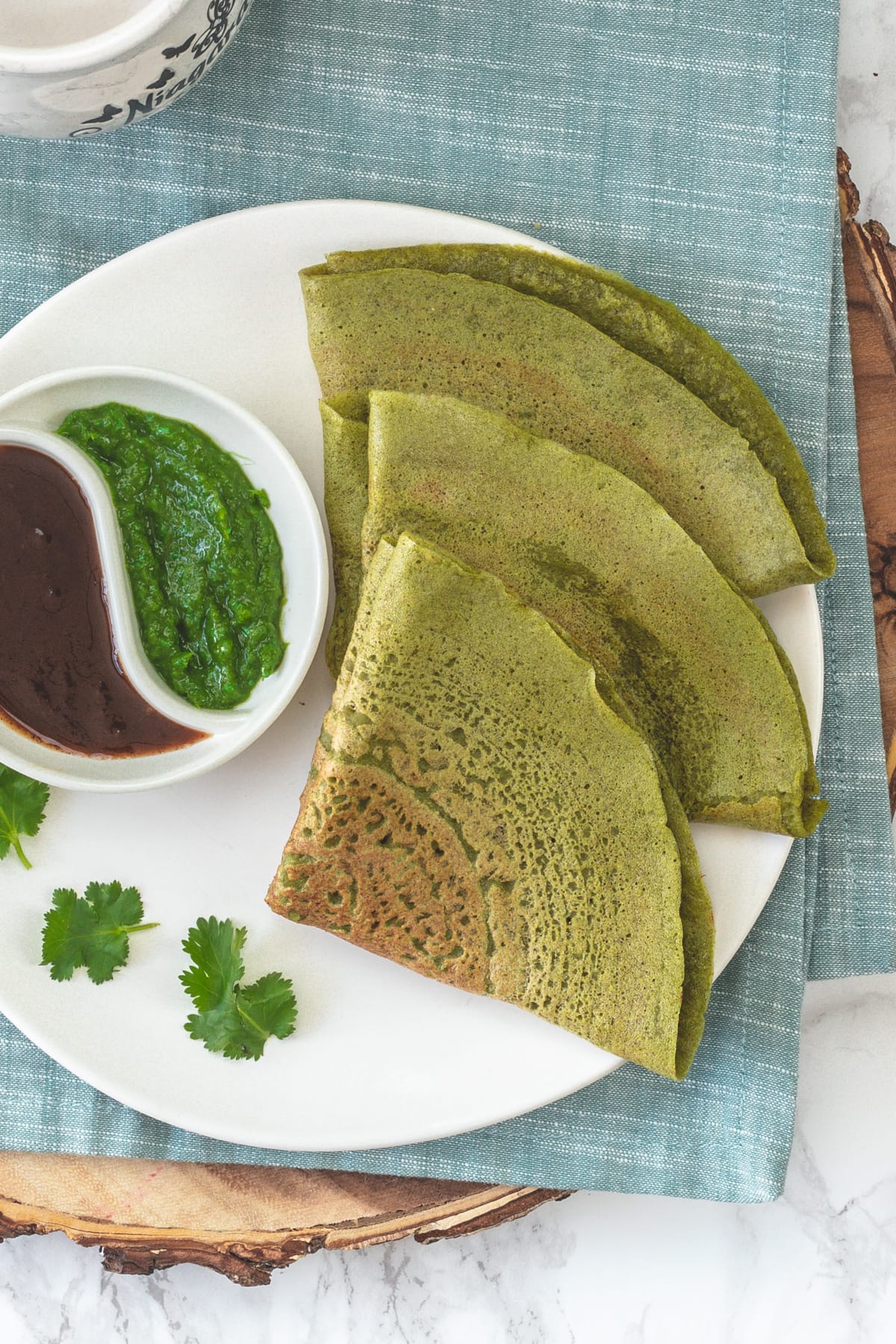 3 triangular folded moong dal chilla with cilantro chutney and tamarind chutney.