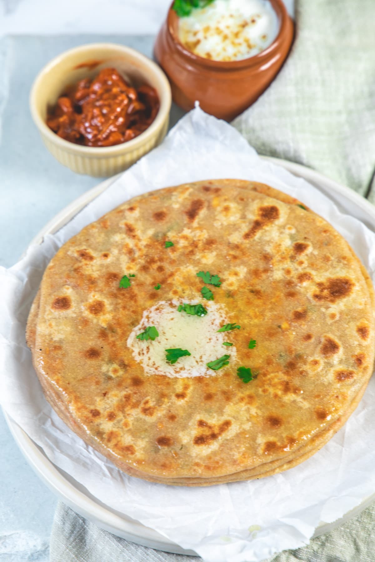 Paneer paratha topped with butter and side of pickle and yogurt.