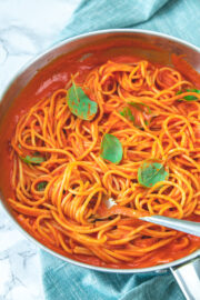 Roasted red pepper pasta in the pan garnished with basil leaves.