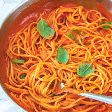 Roasted red pepper pasta in the pan garnished with basil leaves.