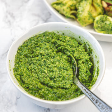Spinach basil pesto in a bowl with a spoon inside.