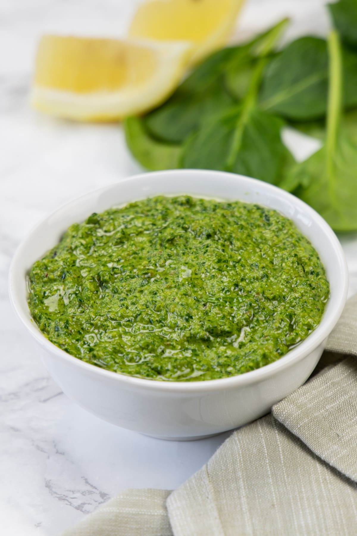 Spinach pesto in a bowl with spinach leaves and lemon slices in the back.