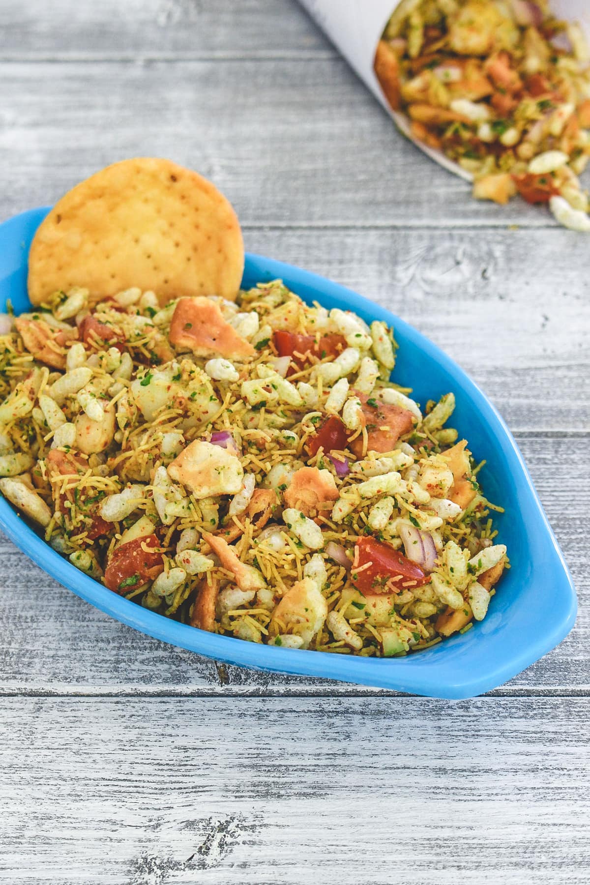 Sukha bhel with papdi on the side and more bhel in paper cone in the back.