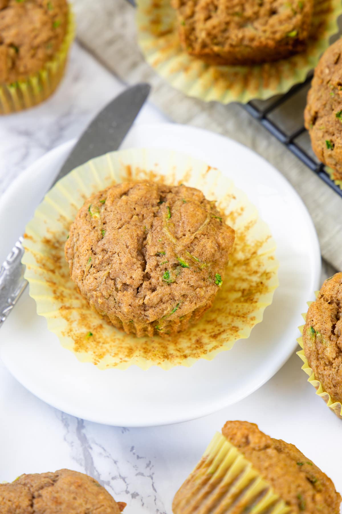 Eggless zucchini muffins with liner removed in a plate and a few more on the side.