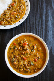 Green moong dal in a bowl and served with rice in a plate in the back.