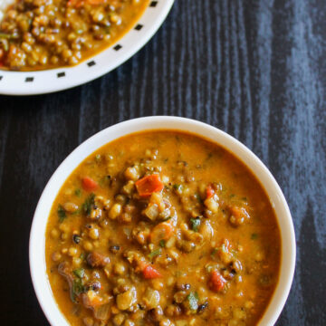 Green moong dal in a bowl and served with rice in a plate in the back.