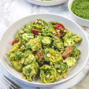 Pesto tortellini salad in two plates with forks on left and a bowl of extra pesto on right.