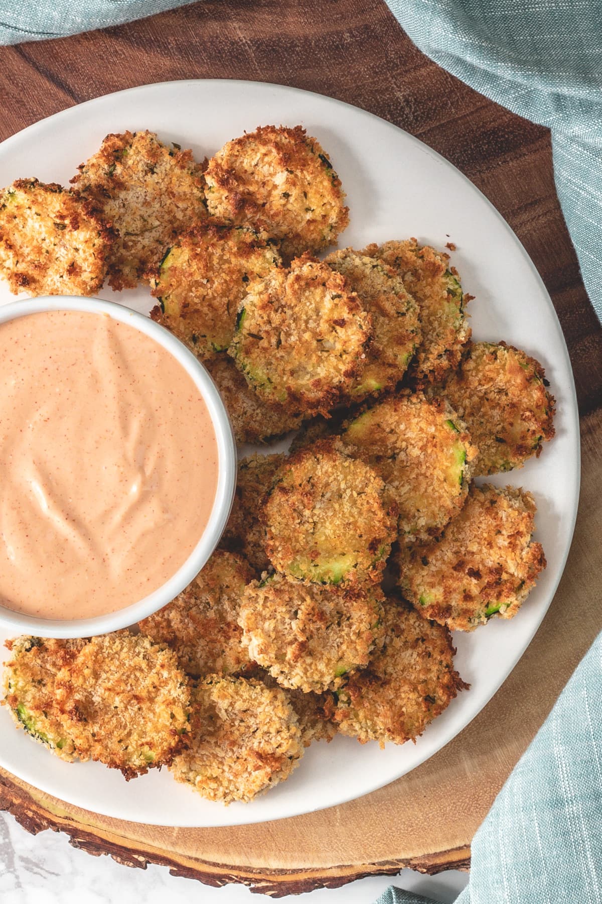 Air fried zucchini chips served with fry sauce on a wooden board.