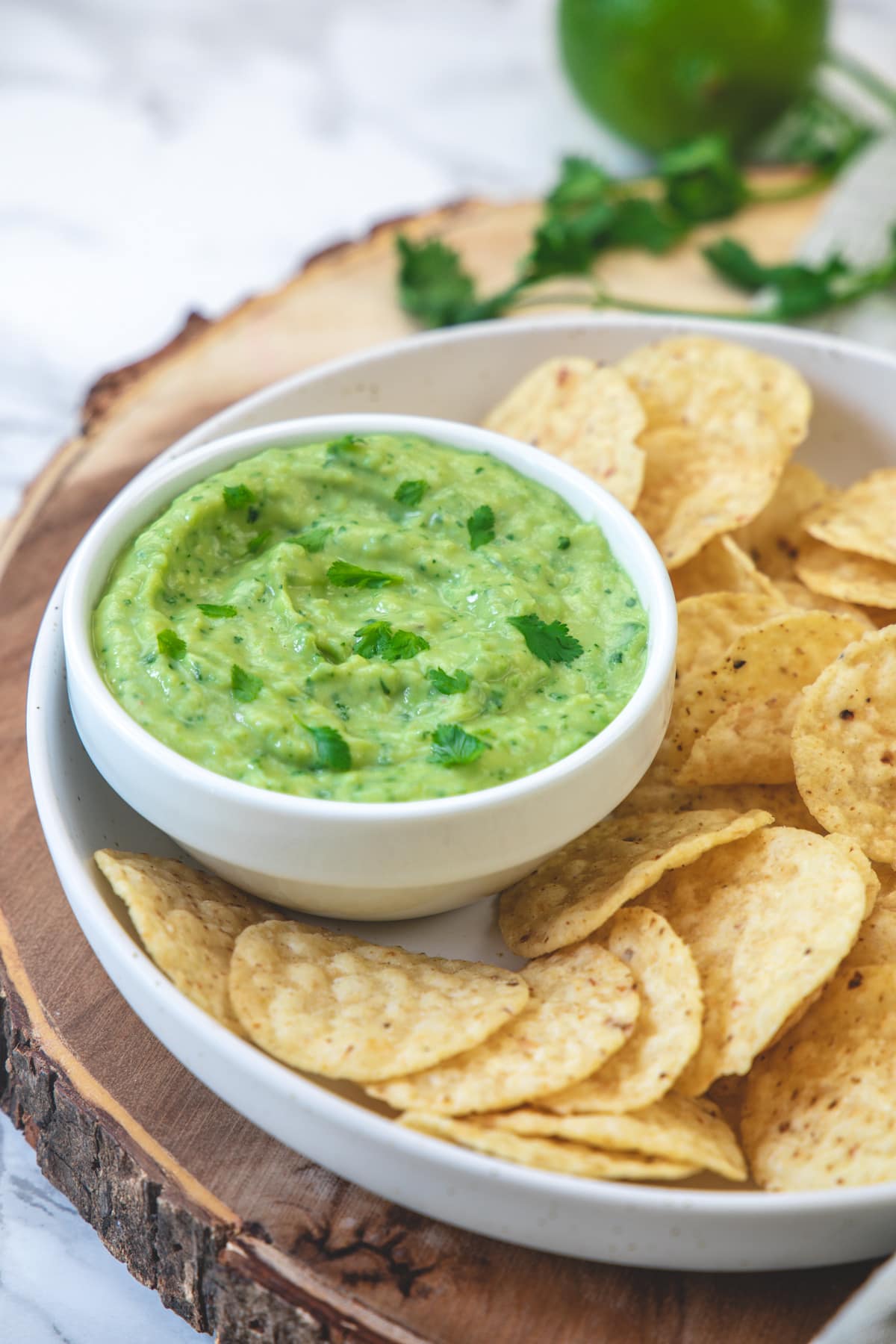 Avocado dip served with round torilla chips on a wooden board.