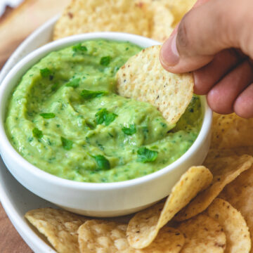 Taking a scoop of avocado dip using a tortilla chip.