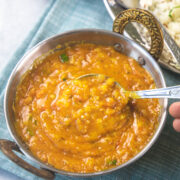 A spoon ful of dal fry is taking away from the serving kadai.