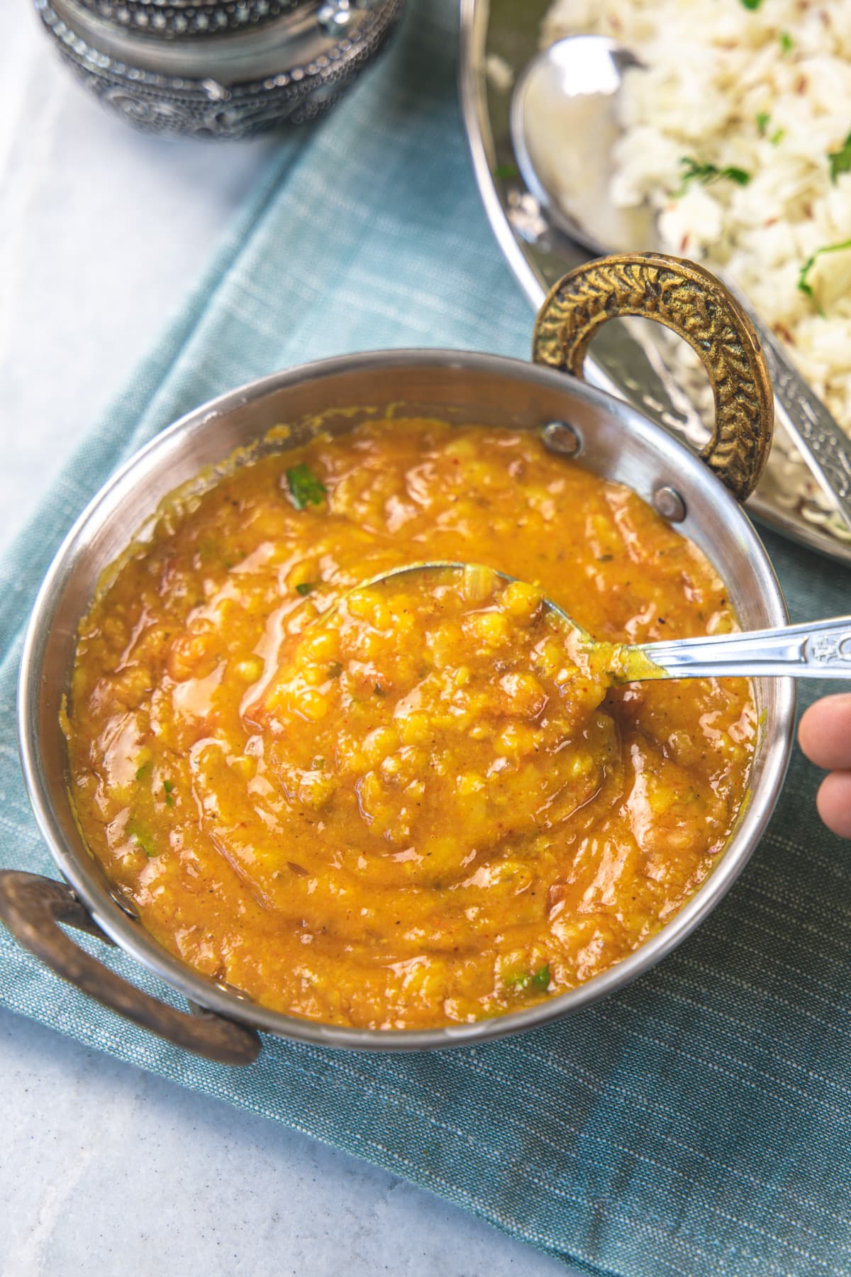 A spoon ful of dal fry is taking away from the serving kadai.