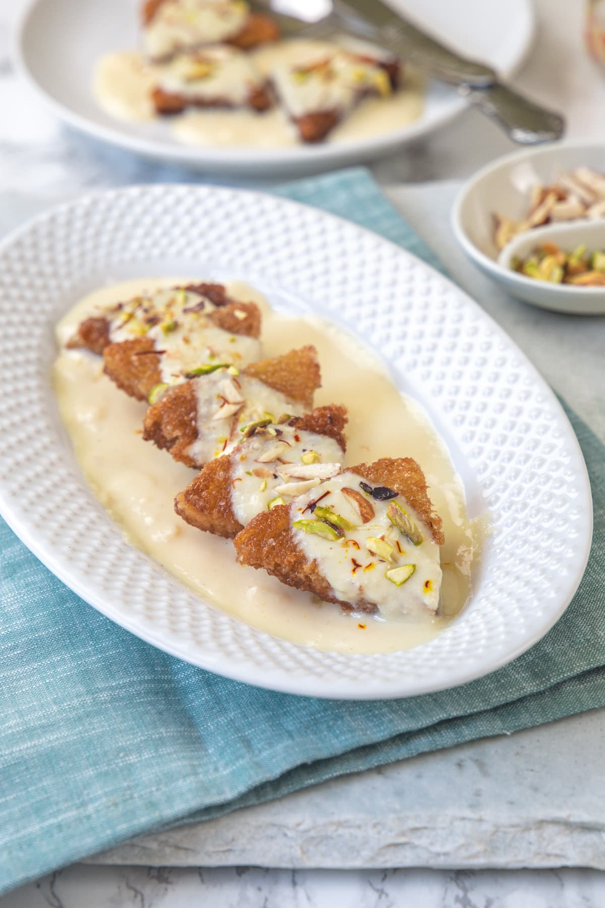 Shahi tukda in an oval plate with nuts and one more plate in the back.