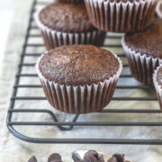 Stack of chocolate muffins on a cooling rack with chocolate chips in front.