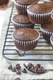 Stack of chocolate muffins on a cooling rack with chocolate chips in front.