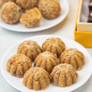 2 plates of churma ladoo with box and flowers in the back.