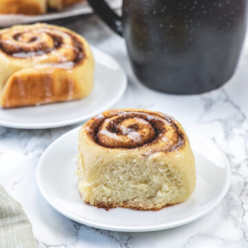 Eggless cinnamon roll served in a plate with more in the back with coffee.