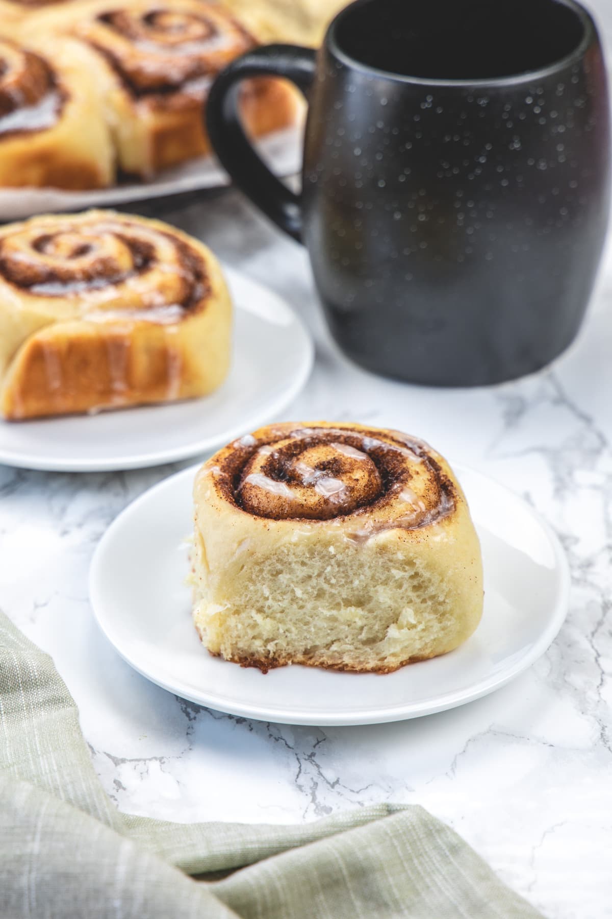 Eggless cinnamon roll served in a plate with more in the back with coffee.