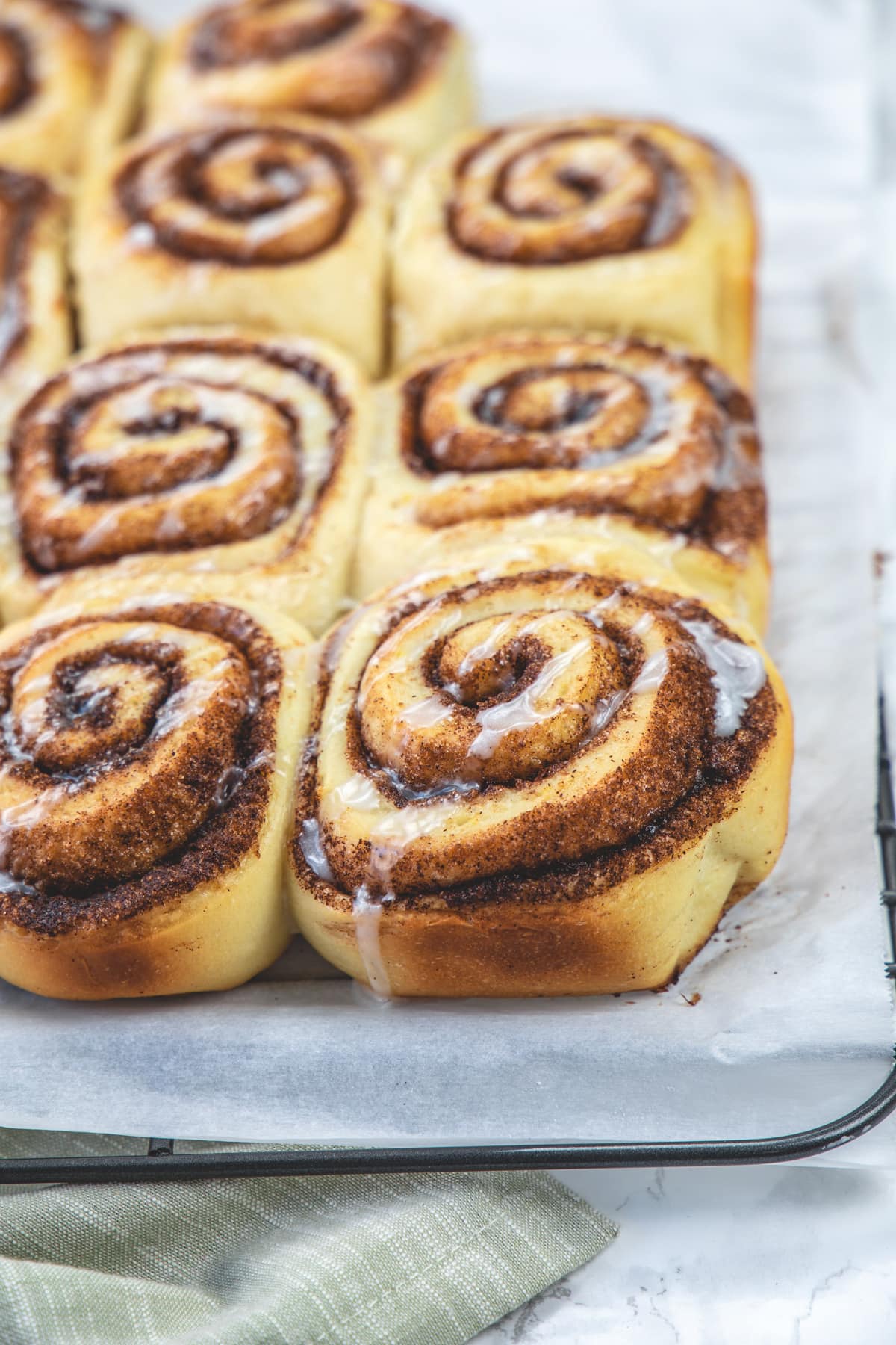 A sheet of cinnamon rolls on a cooling rack with parchment paper.