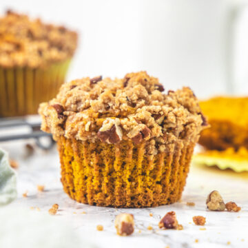 Eggless pumpkin muffin with few more muffins and a cup in the back.