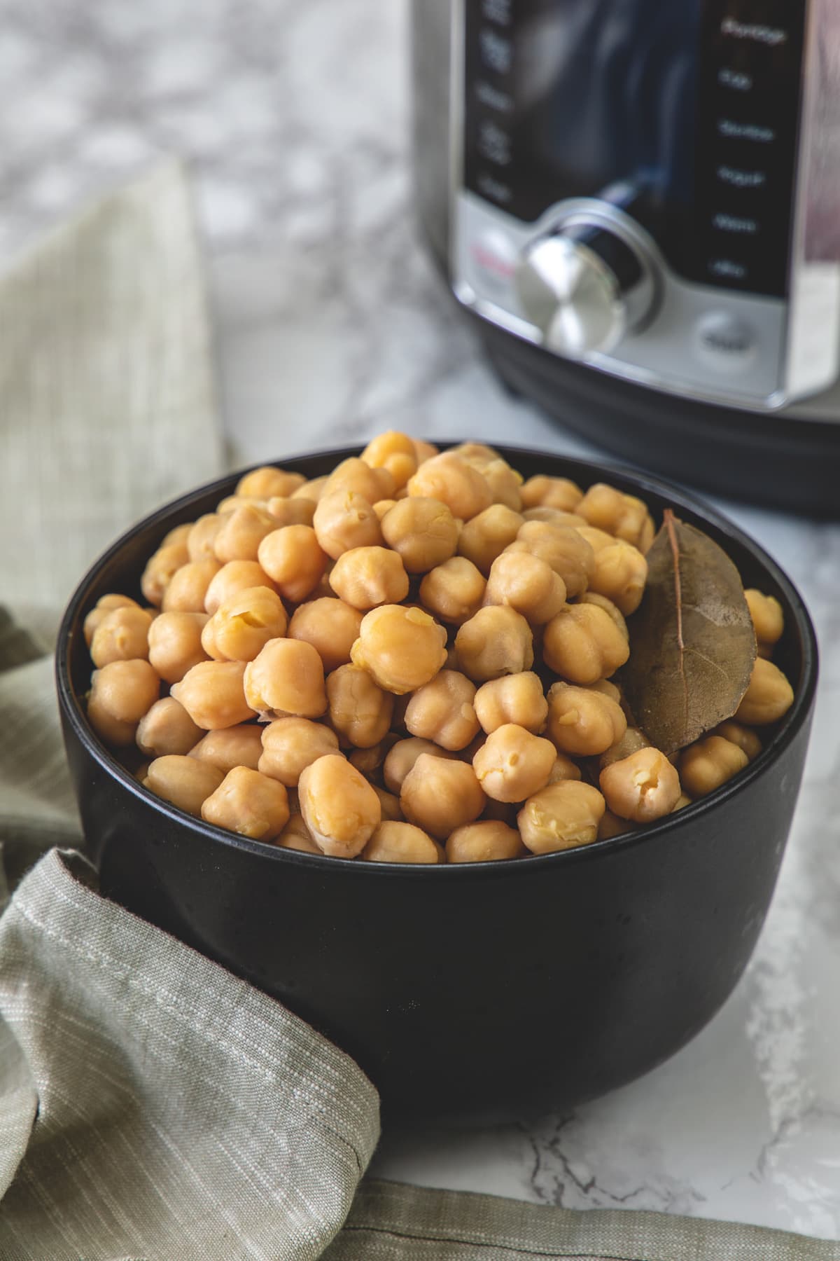 A bowl of cooked chickpeas with napkin on side and instant pot in the back.