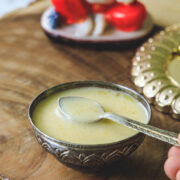 Panchamrut in a silver bowl and taking a spoonful with Ganesh idol in the back.