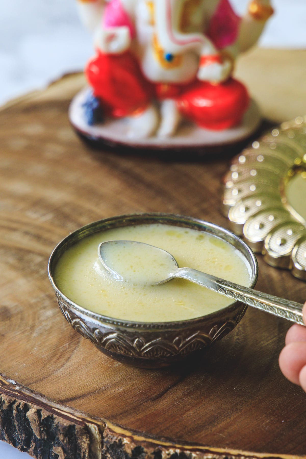 Panchamrut in a silver bowl and taking a spoonful with Ganesh idol in the back.