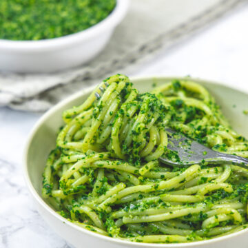 Pesto spaghetti pasta taking with a fork and parsley pesto bowl in the back.