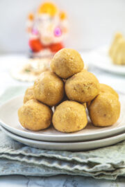 Rava besan ladoo stacked in a plate with ganesh idol in the back.