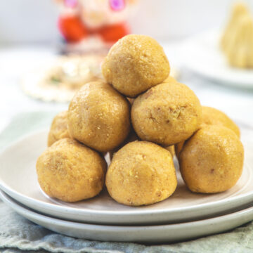 Rava besan ladoo stacked in a plate with ganesh idol in the back.