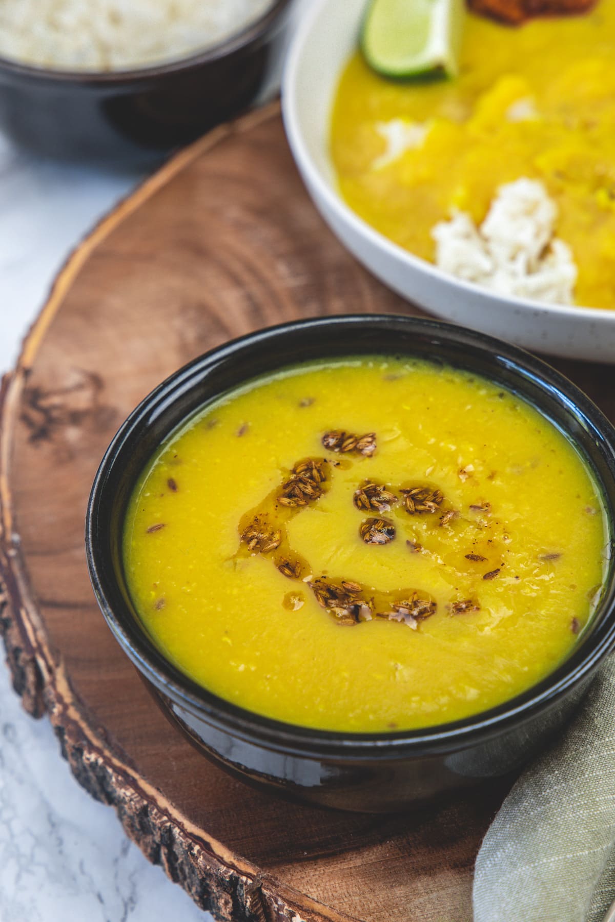 Varan in a black bowl with rice in another bowl and varan bhaat in a plate.