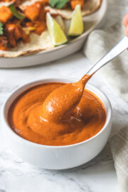 Taking a spoonful of chipotle sauce from a bowl with taco plate in the back.