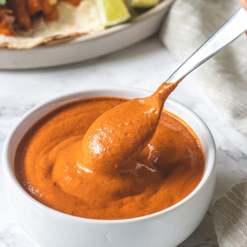 Taking a spoonful of chipotle sauce from a bowl with taco plate in the back.