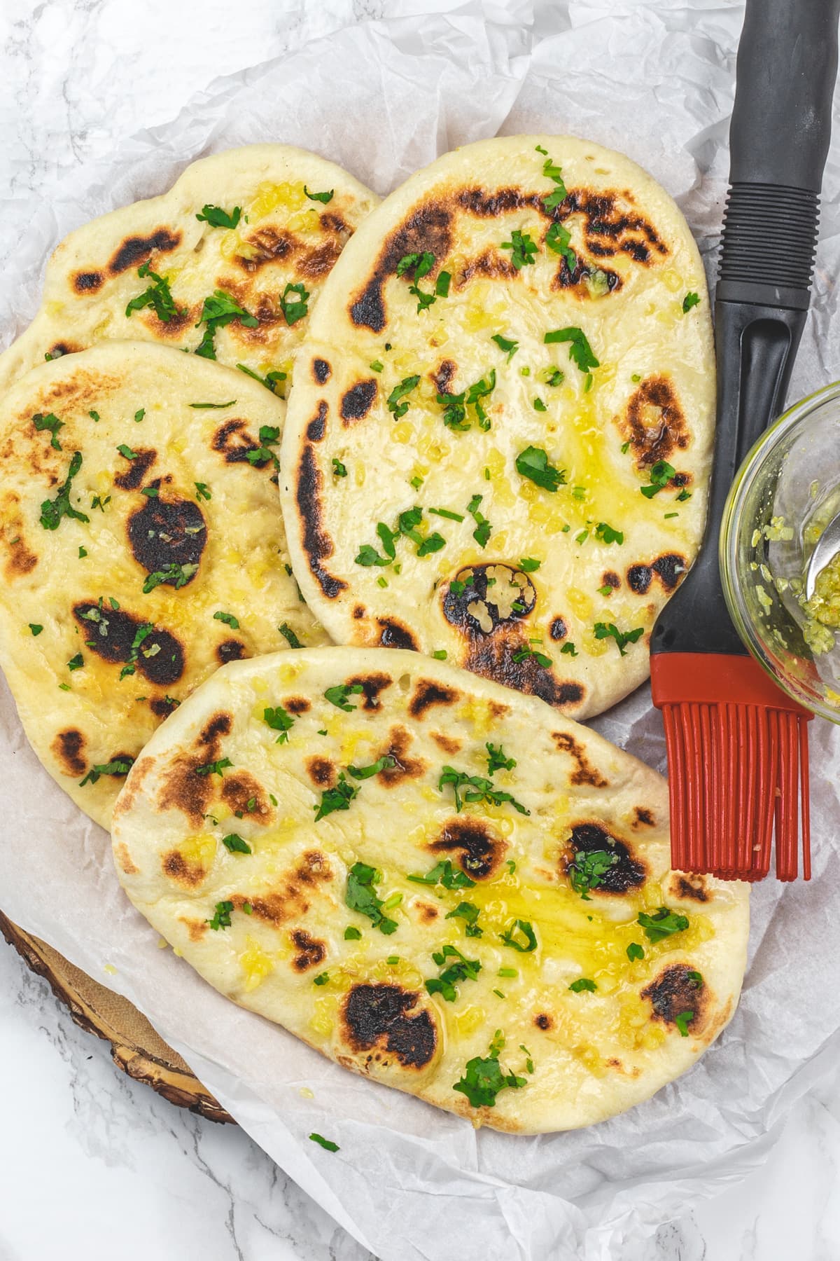 4 garlic naan on a parchment paper with pastry brush on the side.