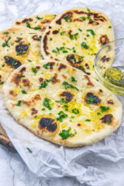 3 garlic naan on a parchment paper with garlic ghee bowl on the side.